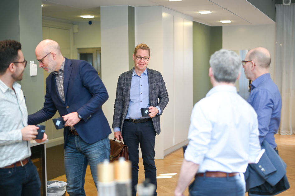 En grupp män som står med kaffekopar i handen och samtalar.