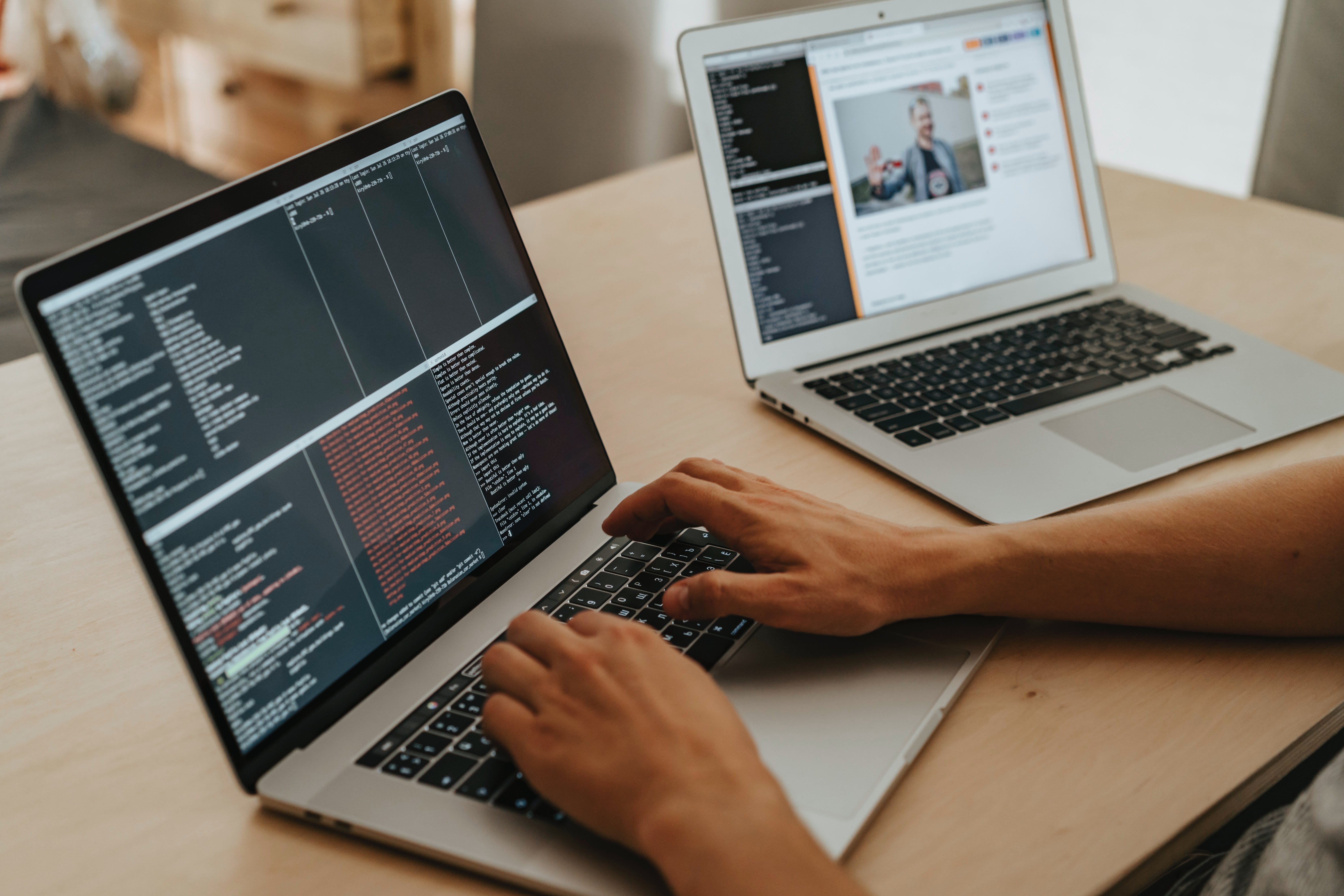 Två laptops står på ett bord och en person som programmerar på ena.