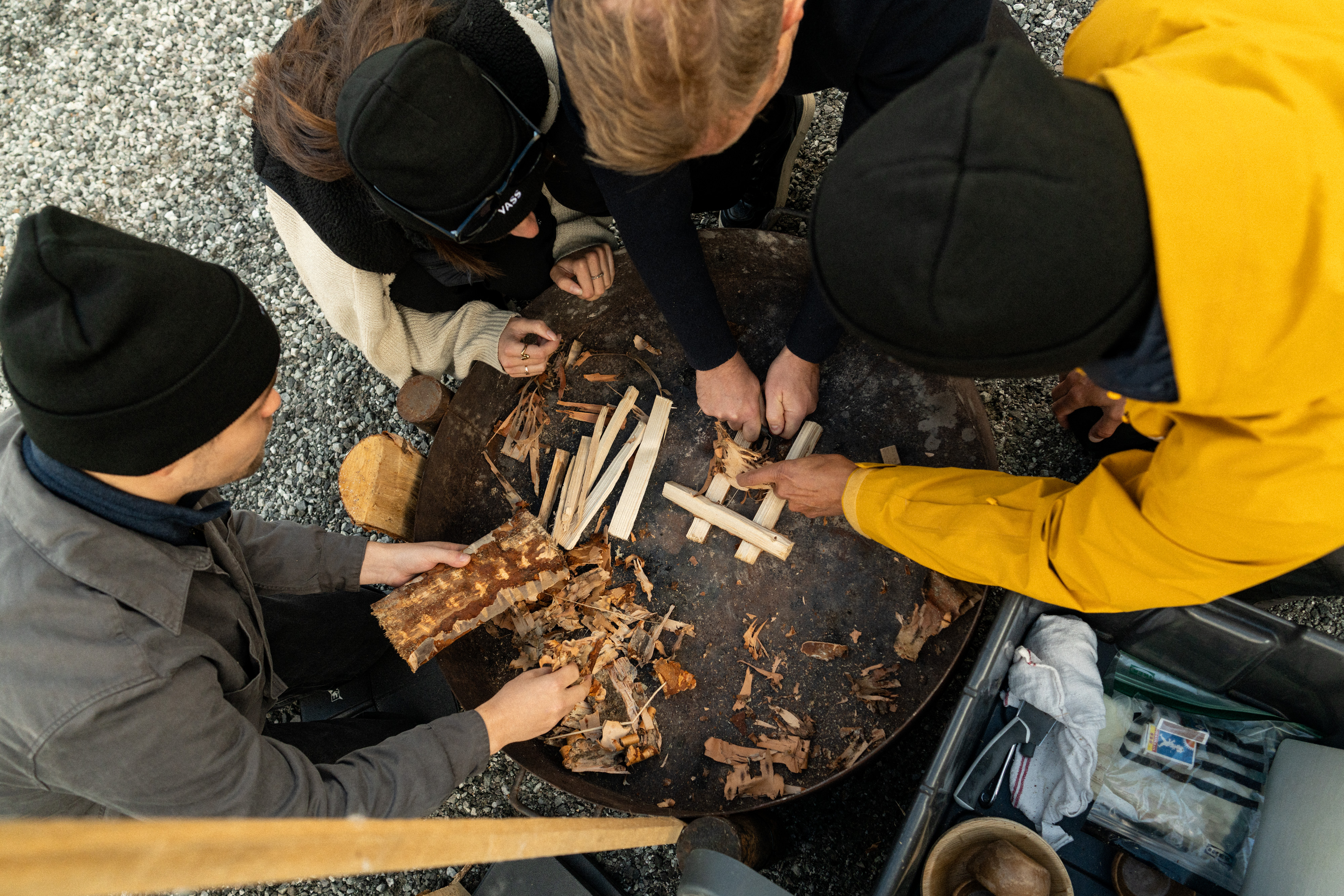 Flera människor i friluftskläder samarbetar kring en grillplats i fjällmiljö 