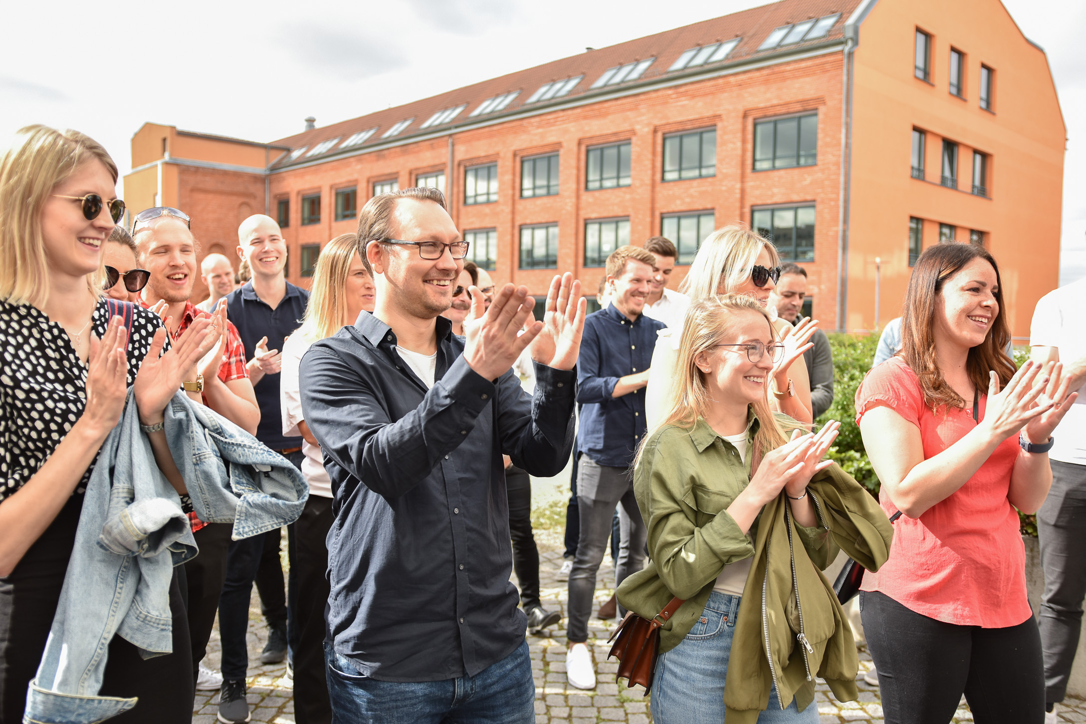 En grupp glada människor står utomhus och klappar händerna.