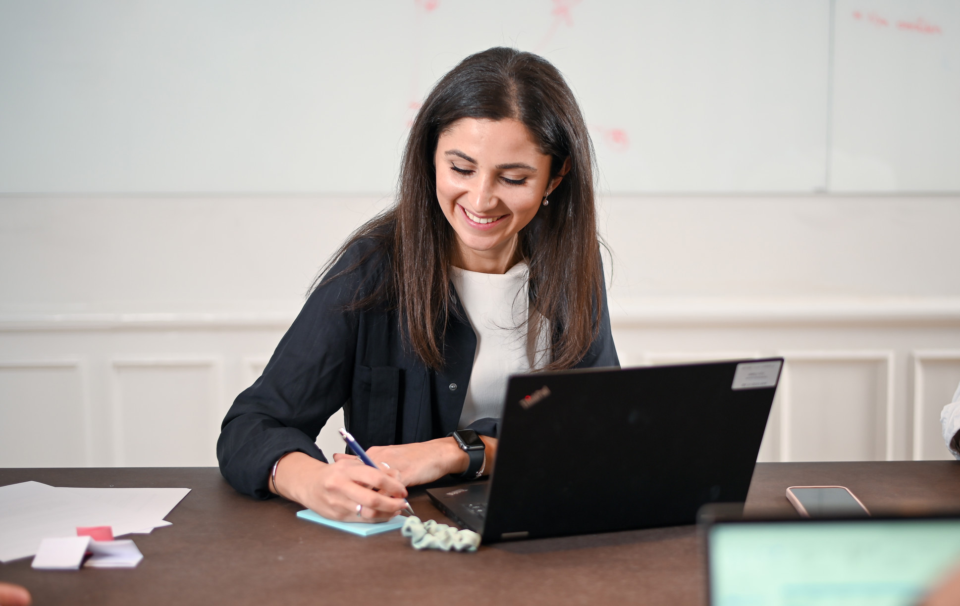 En kvinna som sitter vid ett bord med en bärbar dator och skriver på en post-it lapp.