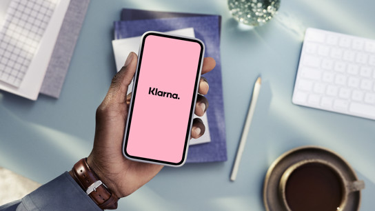 En hand som håller en mobiltelefon och på skärmen står det Klarna.