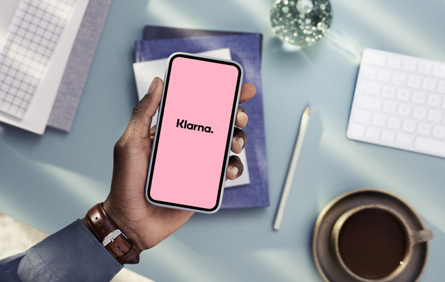 En hand som håller en mobiltelefon och på skärmen står det Klarna.