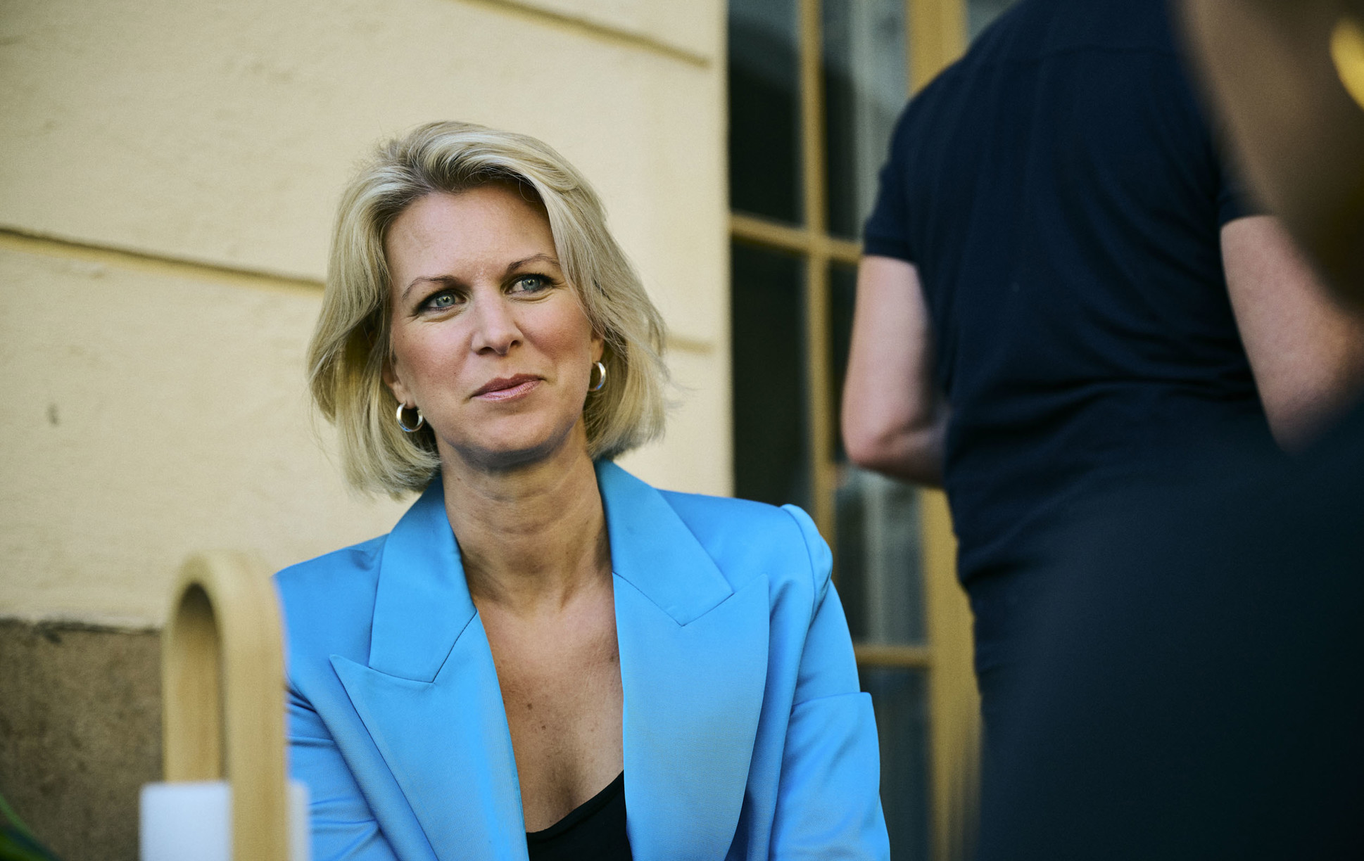 En bild på en kvinna med blå kavaj utomhus som sitter ner ock kollar någonstans mot kamerans håll.