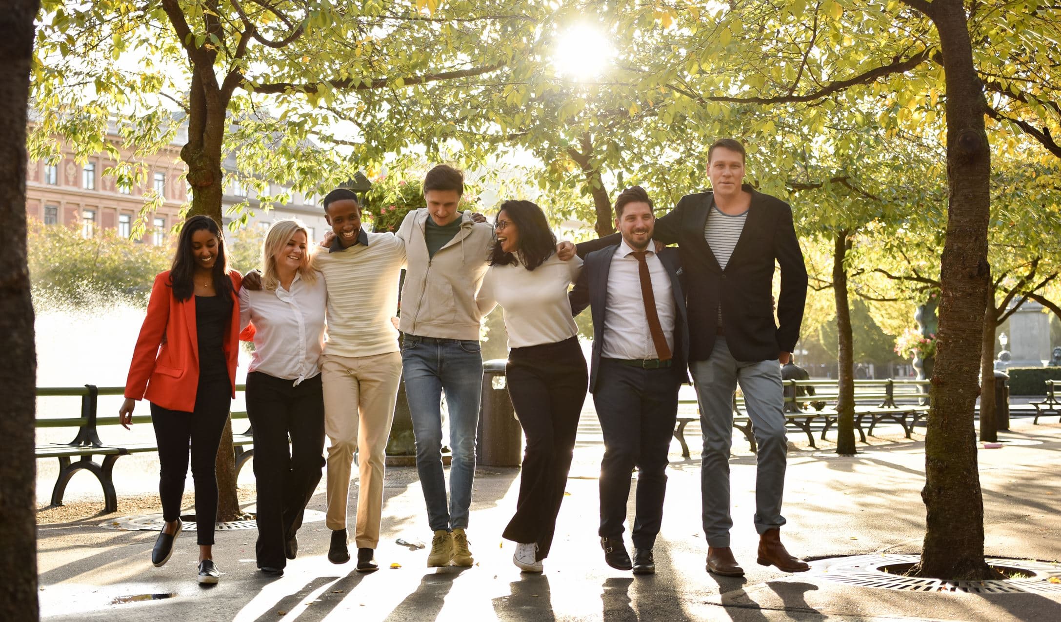 En grupp glada människor poserar för en bild i en park med solen bakom sig.